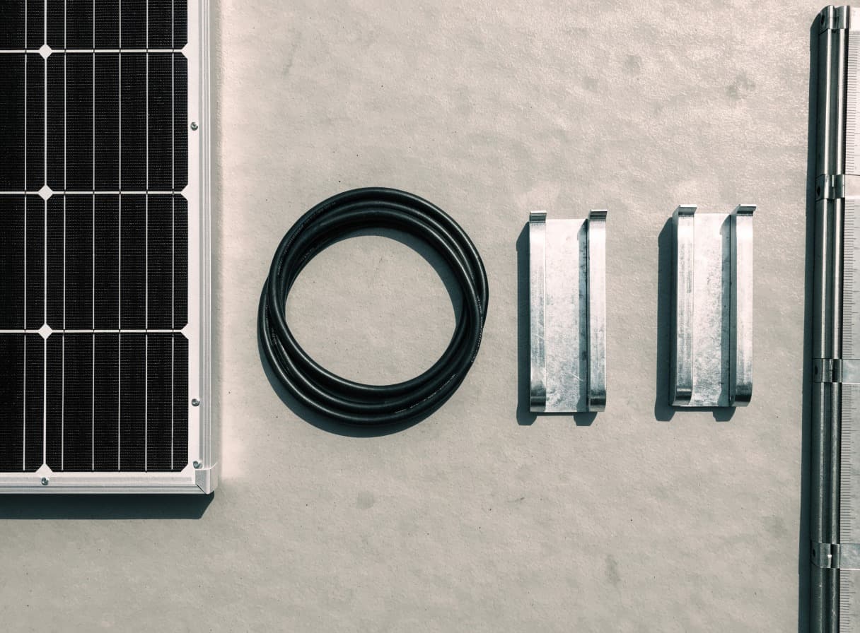 Modulecke, Solarkabel, zwei Montageklemmen und ein Zollstock nebeneinander auf einer Werkbank