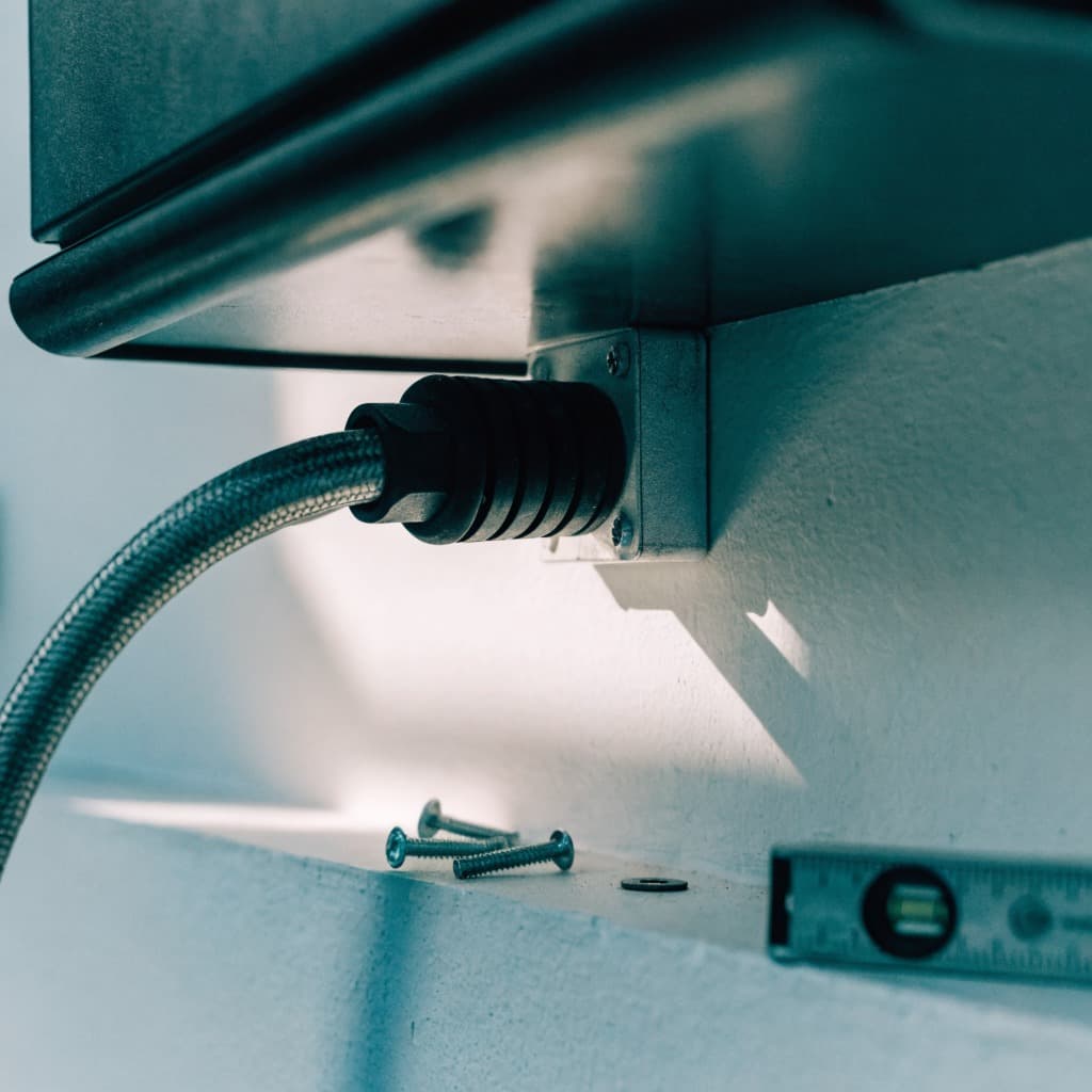 Unterseite einer Wandladestation, ein graues Mantelleitungskabel läuft durch eine Verschraubung in eine Abzweigdose